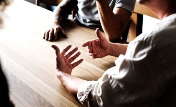 Tres personas hablan alrededor de una mesa / RAWPIXEL.COM